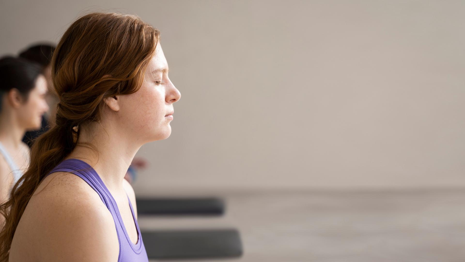 Femme assise, les yeux fermés, en pleine méditation, dans une posture de relaxation, illustrant une séance de sophrologie où l’attention est portée sur la respiration et le calme intérieur.