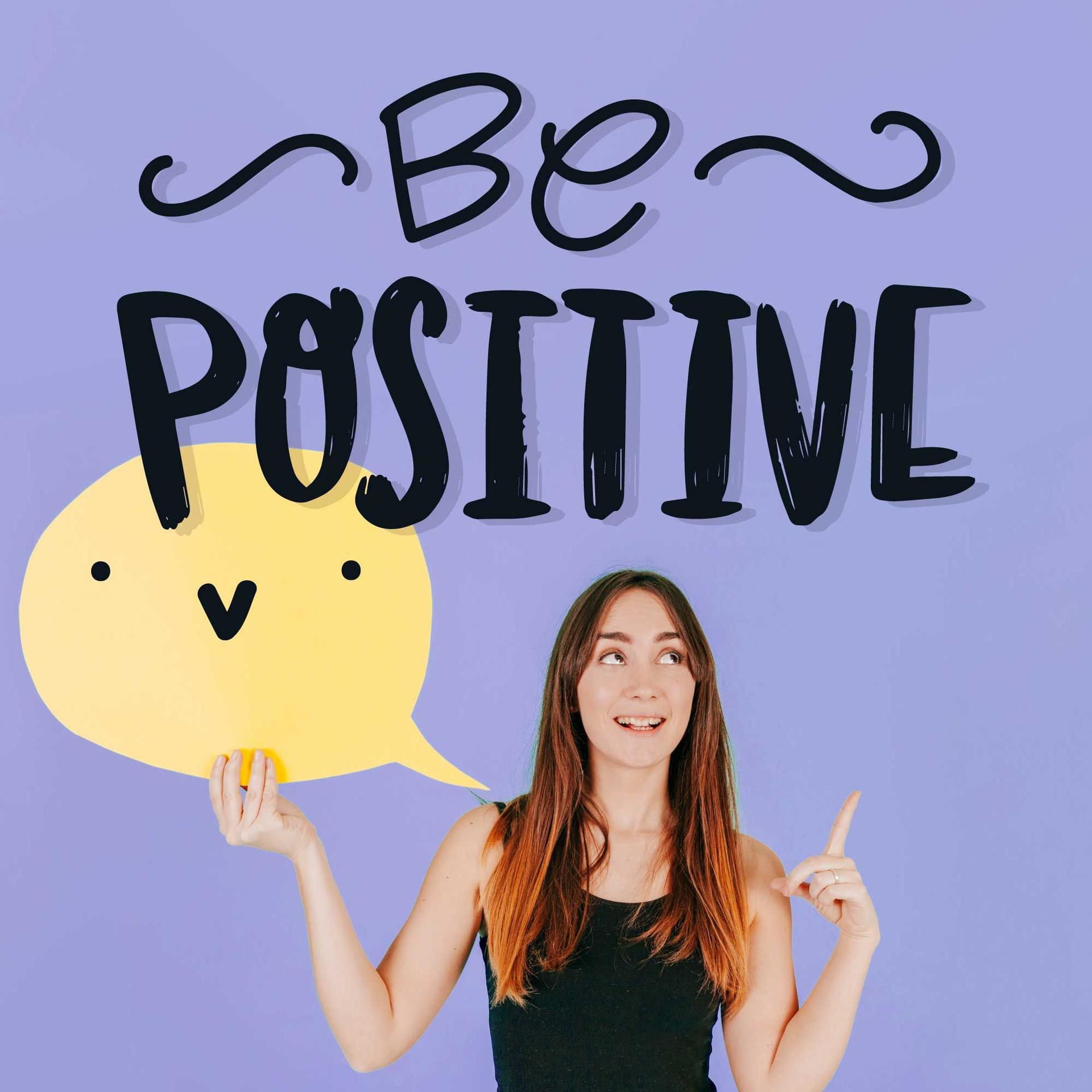 Femme souriante tenant un panneau jaune avec le message 'Be Positive', représentant la joie et l'optimisme de la pensée positive