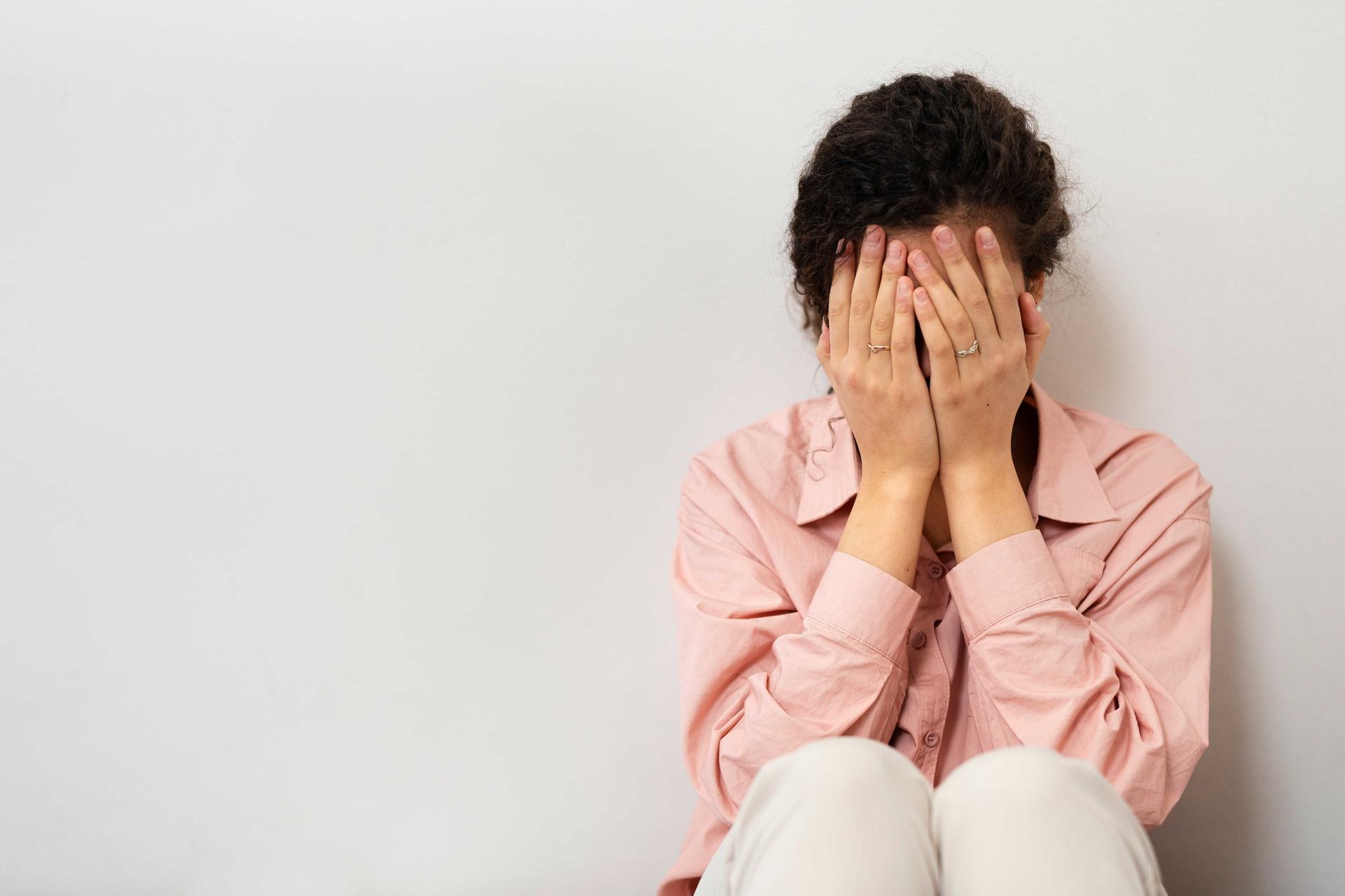 Femme assise, le visage caché dans ses mains, exprimant une forte anxiété et un stress émotionnel.