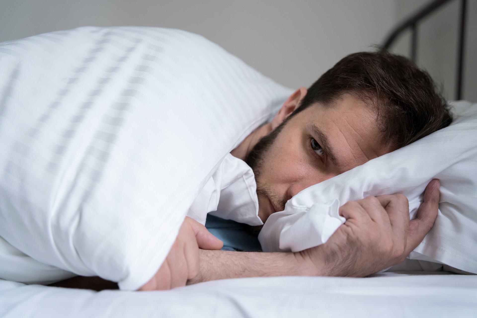 Un homme allongé dans son lit, l'air fatigué, le regard vide, illustrant les difficultés de sommeil et la fatigue diurne fréquentes chez les personnes souffrant d'apnée du sommeil