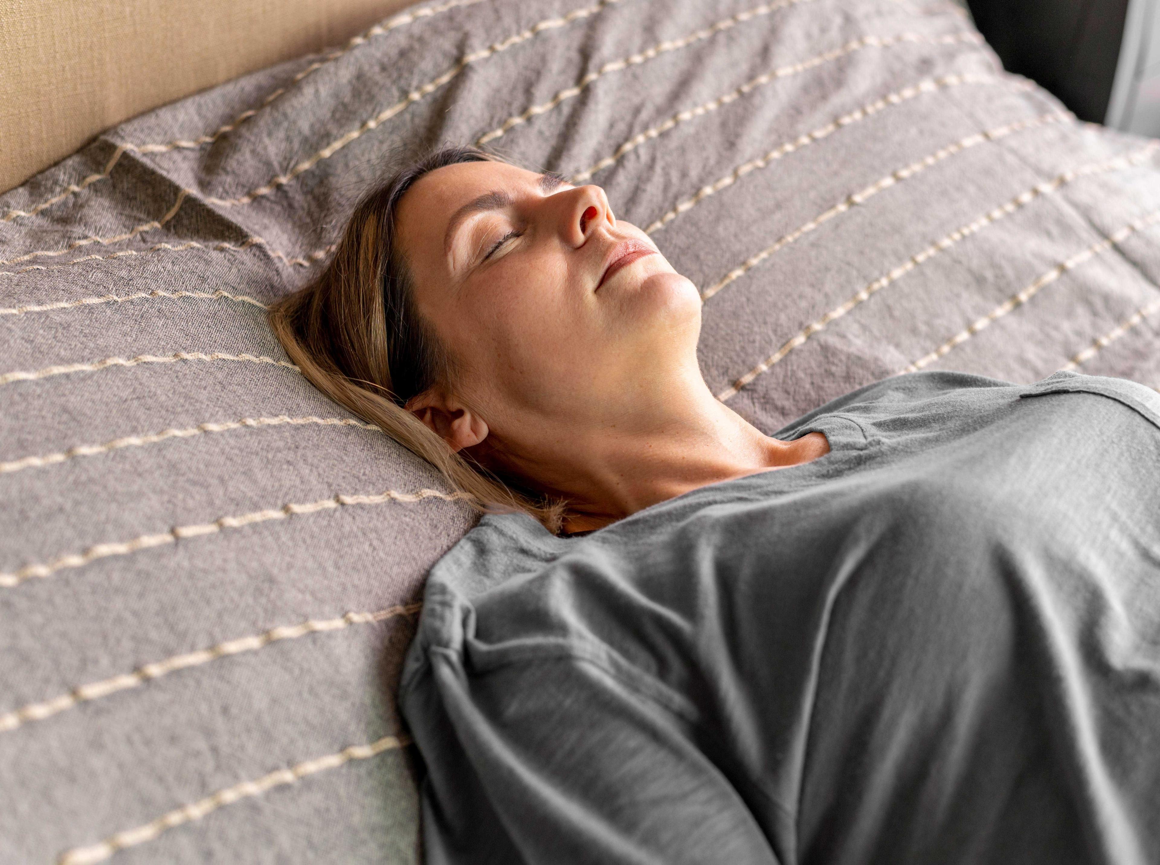 Femme allongée sur un lit, les yeux fermés, illustrant une phase de sommeil léger dans un environnement calme et propice à la détente
